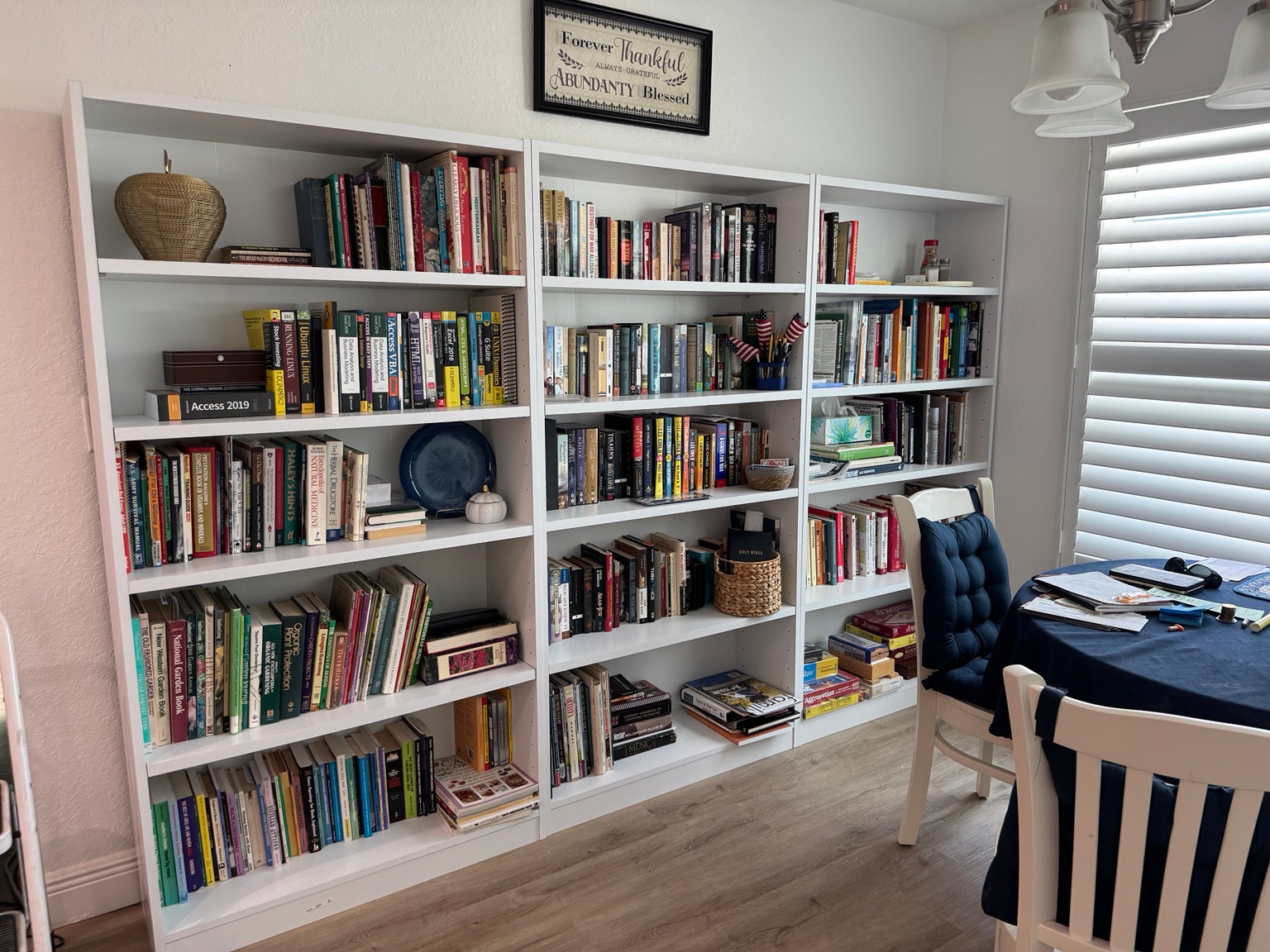 Three white bookshelves arranged along a wall and filled with books